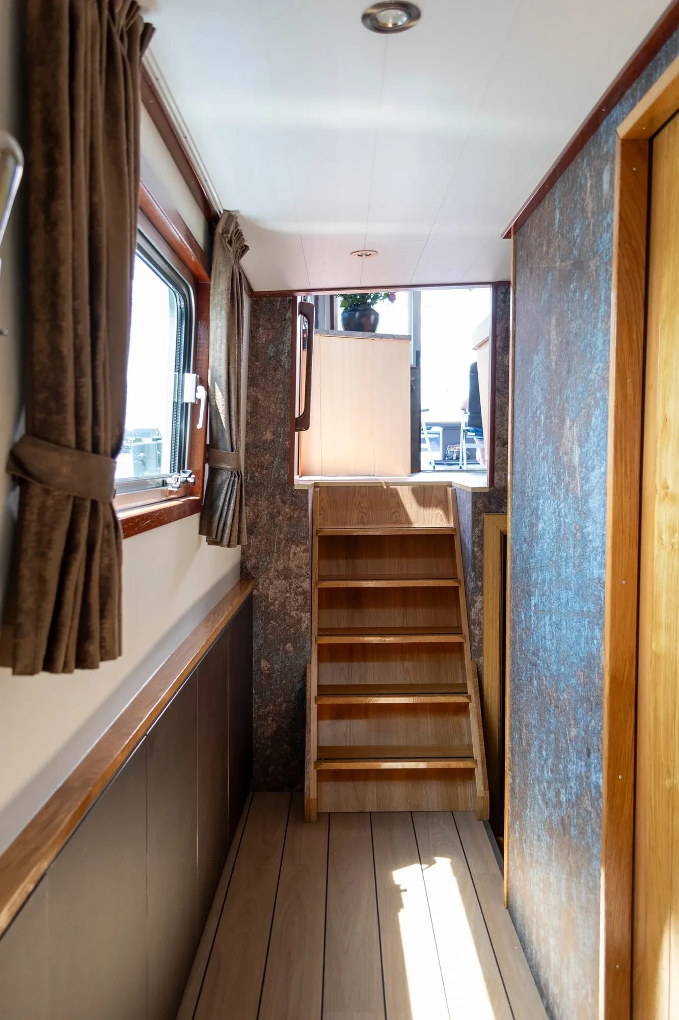 Houten trap en doorgang met gordijnen aan boord van Sadilé.